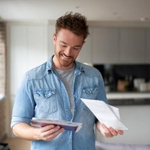 Smiling man reading papers from an opened envelope.